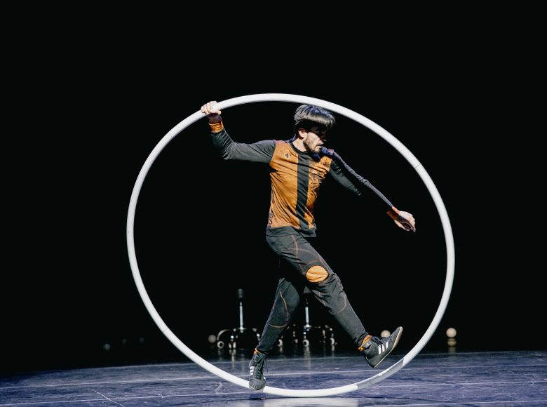 Zdjęcie przedstawia akrobatę na scenie stojącego w wielkim kole