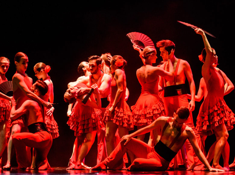 Zdjęcie. Przedstawia tancerzy i tancerki w kostiumach w stylu latynoskim. Pada na nich czerwone światło.