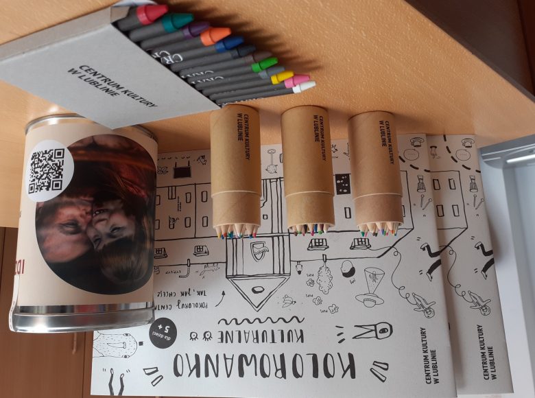 [Zdjęcie przedstawia kolorowanki, kredki i puszkę na datki leżące na stole