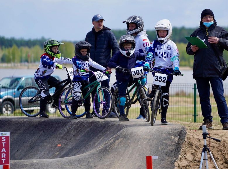 [Zdjęcie przedstawia dzieci startujące w wyścigu kolarskim. Stoją na starcie.