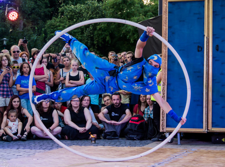 Zdjęcie. Mężczyzna w niebieskim kostiumie. Wykonuje akrobacje z obręczą.