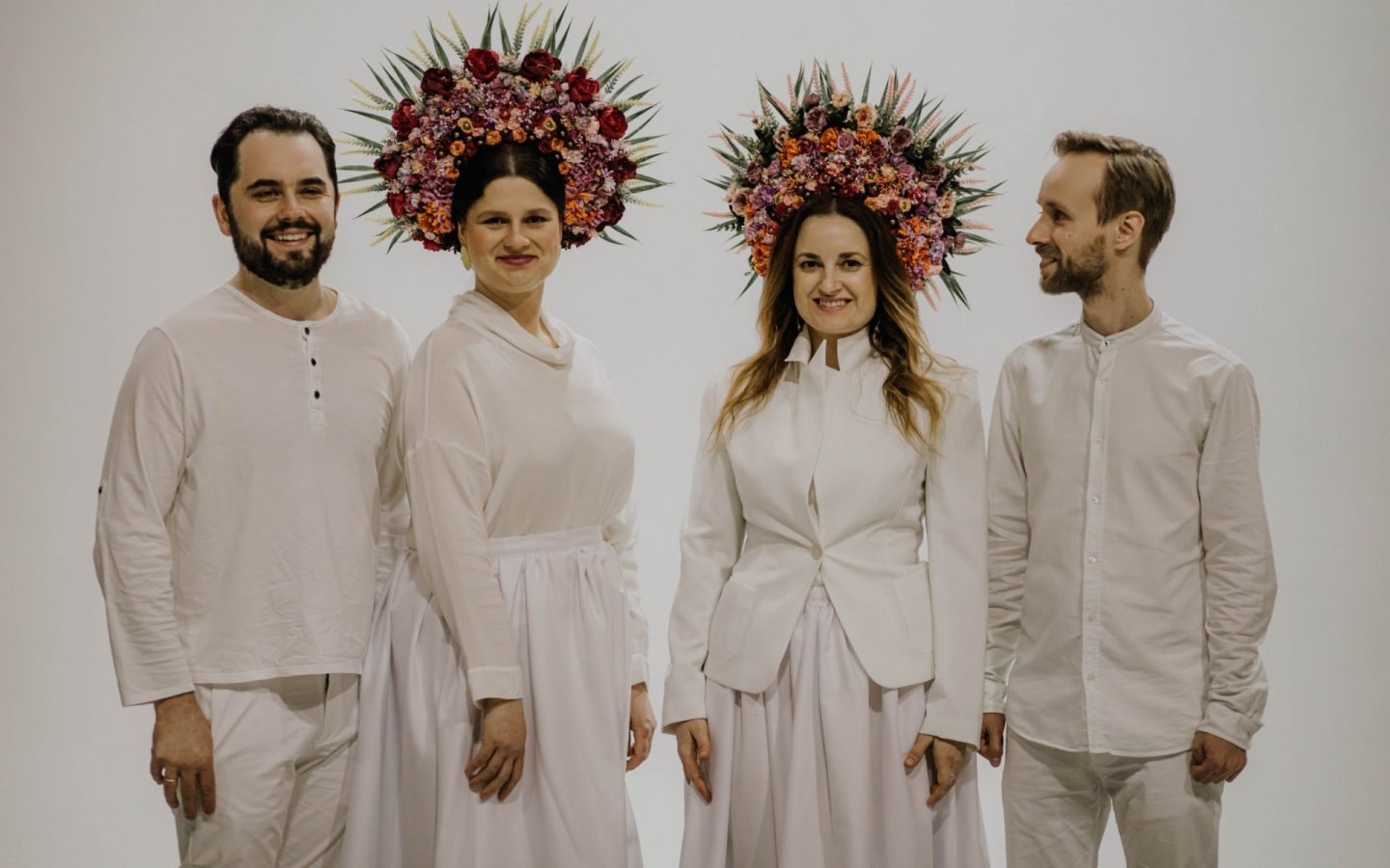 Zdjęcie czterech członków zespołu Dagadana. Wszyscy ubrani są na biało. Kobiety pośrodku mają na głowach wianki ze świeżych kwiatów