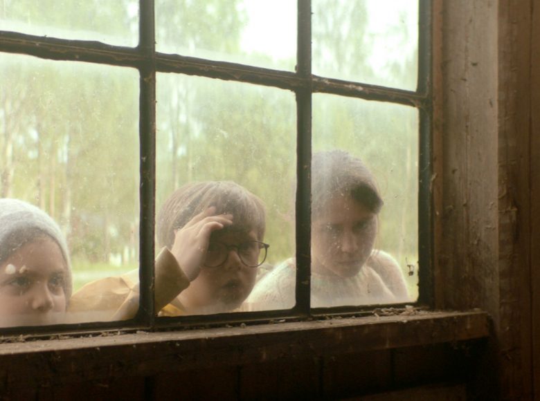 [Kadr z filmu. Zdjęcie przedstawia troje dzieci zaglądających przez okno]