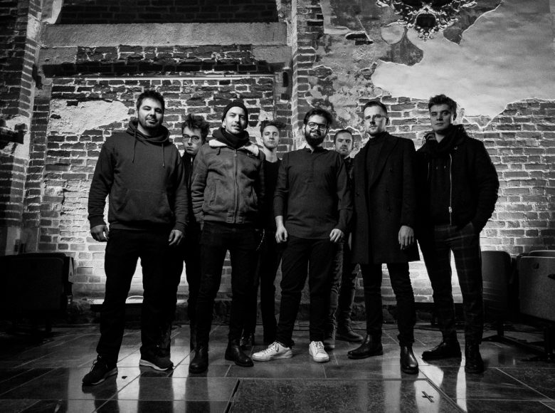 [osmiu młodych mężczyzn stojących w dwóch rzędach na ceglanym tle, patrzą wprost w obiektyw]