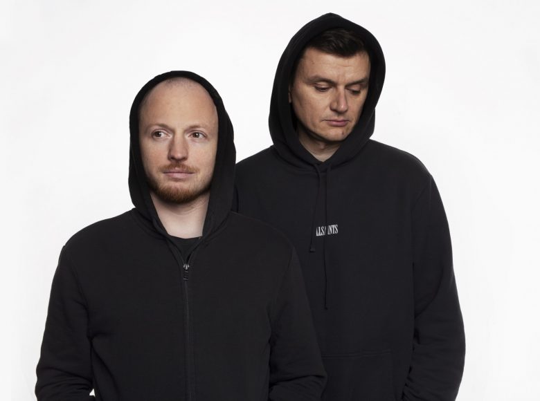 Dwóch stojących mężczyzn w czarnych bluzach z kapturem na białym tle