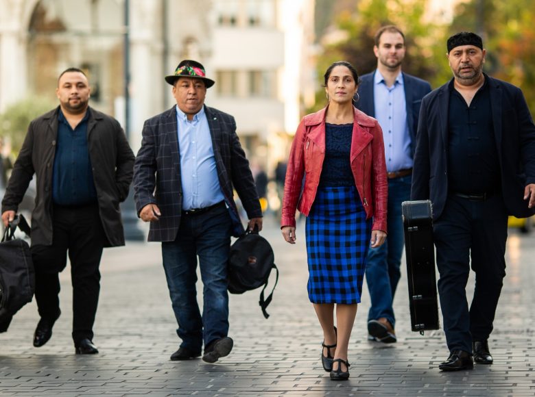 Członkowie zespołu Romengo. Czterech mężczyzn idzie ulicą. Niosą instrumenty muzyczne w futerałach. Towarzyszy im kobieta.