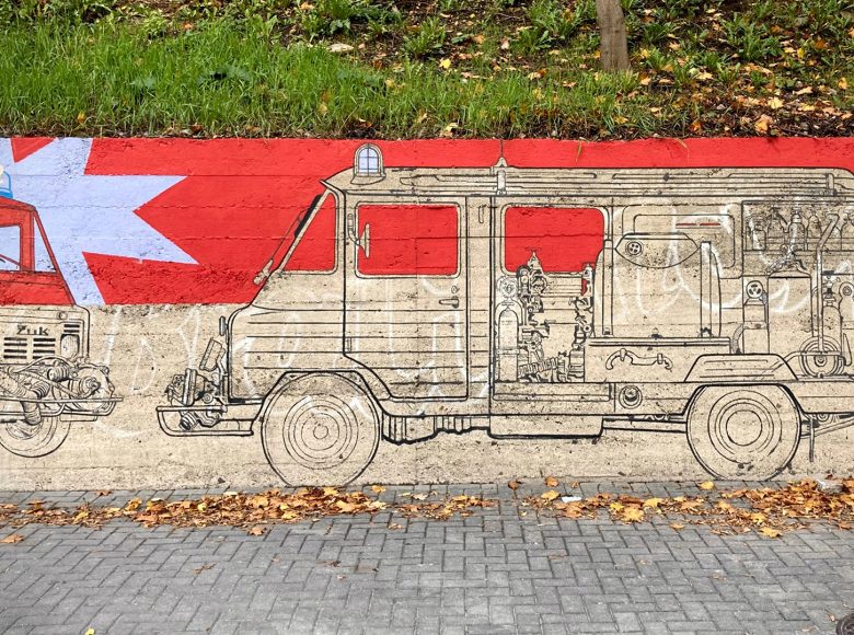 Mural namalowany na ulicznym murze. Przedstawia samochody marki Żuk z Lubelskiej Fabryki Samochodów Ciężarowych.