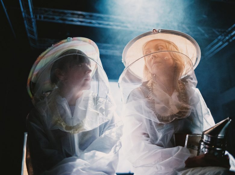 Dwie kobiety w strojach pszczelarskich. Siedzą, patrzą na siebie.