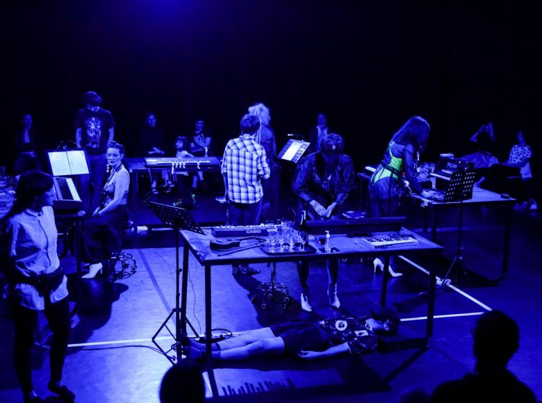 Grupa ludzi wokół 4 podestów ustawionych w formie kwadratu na środku zdjęcia. Sytuacja chaotyczna – część osób stoi za podestami, 2 osoby chodzą w środku, kilka osób siedzi dookoła.