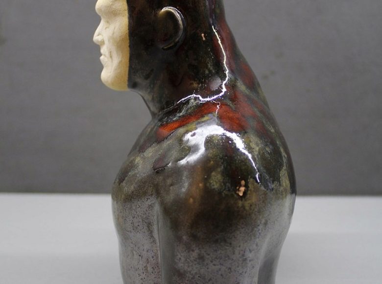 Zdjęcie. Przedstawia rzeźbę. To popiersie mężczyzny. Rzeźba jest ustawiona bokiem. Tło jasne, jednolite.