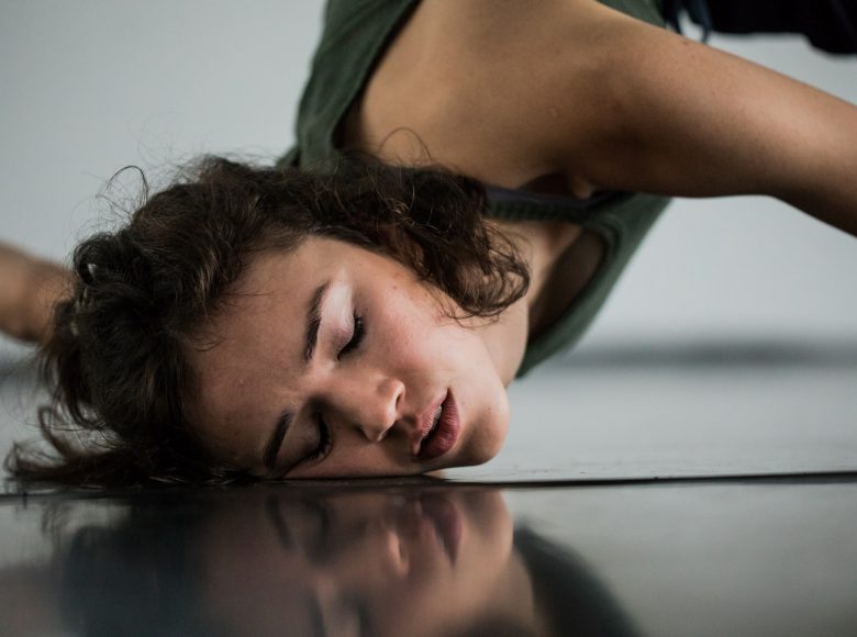 Zdjęcie. Tancerka dotyka twarzą ziemi. Ma zamknięte oczy.