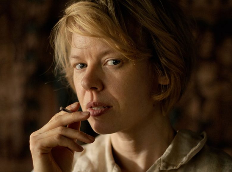 Kadr z filmu. Zbliżenie na kobietę, która patrzy prosto w obiektyw i pali papierosa.