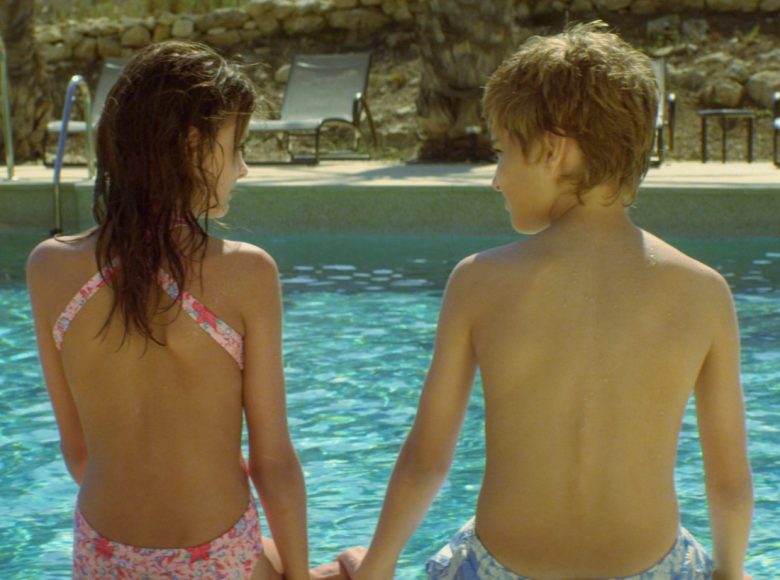 [ Kadr z filmu. Dwoje nastolatków siedzi na krawędzi basenu, odwróceni do nas plecami. Patrzą na siebie. ]