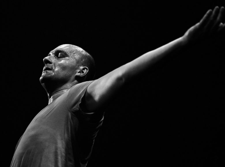 Zdjęcie. Zbliżenie na mężczyznę, wypina do przodu pierś, ma zamknięte oczy i skupiony wyraz twarzy.