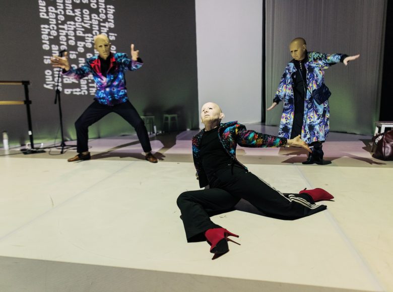 Zdjęcie. Scena ze spektaklu "W moim początku jest mój kres". Przedstawia trzy osoby w identycznych maskach, przedstawiających twarz starego, łysego mężczyzny.