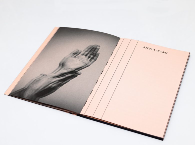 Zdjęcie. Zbliżenie na otwartą książkę. Jedna strona jest kremowa, z lewej strony przecinają ją trzy czarne, pionowe pasy. Tytuł: Sztuka Troski. Na drugiej stronie znajduje się czarno-białe zdjęcie wyciągniętych dłoni.