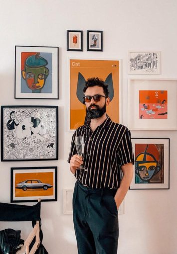 Młody mężczyzna stoi na tle ściany z kolorowymi grafikami.