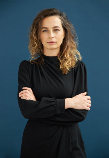 Młoda kobieta stoi z rękami skrzyżowanymi na piersiach, patrzy w obiektyw.