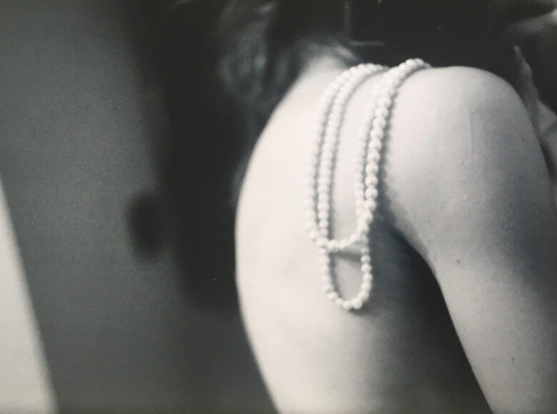 Czarno białe zdjęcie. na zbliżeniu nagie plecy kobiety. Na jej ramieniu wisi sznur pereł.