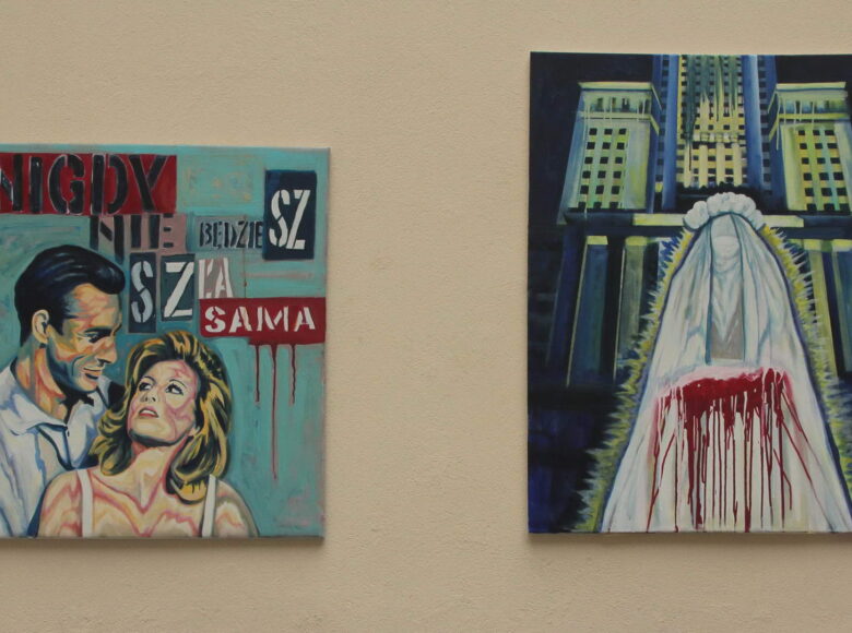 Zdjęcie. beżówa ściana, na niej dwa obrazy. Jeden przedstawia patrzących na siebie mężczyznę i kobietę. Nad nimi drukowanymi literami napis: Nigdy nie będziesz szła sama. Tło jest niebieskie. Drugi obraz przedstawia kobieca postać bez twarzy w białych szatach i welonie. Część szaty jest zaplamiona czerwoną barwą, przypomina to rozlewająca się krew. Za postacią znajduje się wielki budynek z kolumnami.