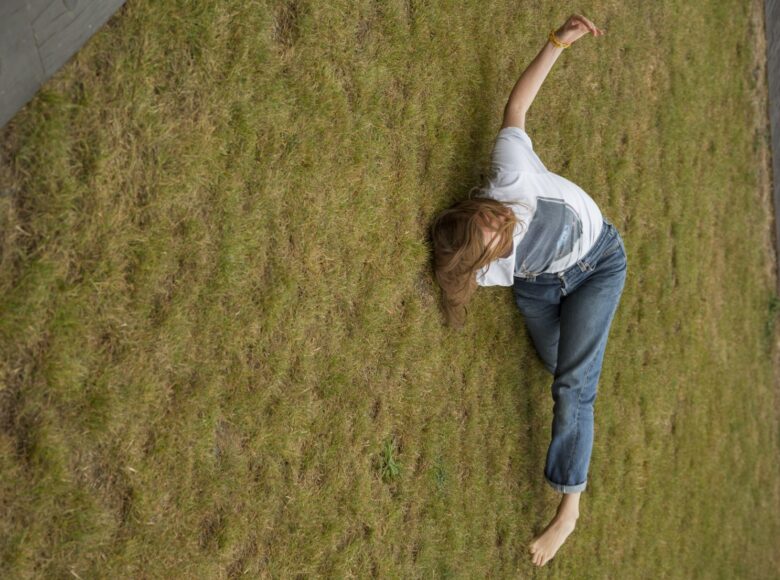 Zdjęcie. kobieta w dżinsach i jasnym podkoszulku leży na trawie bokiem, ciężar ciała opiera na jednym ramieniu.