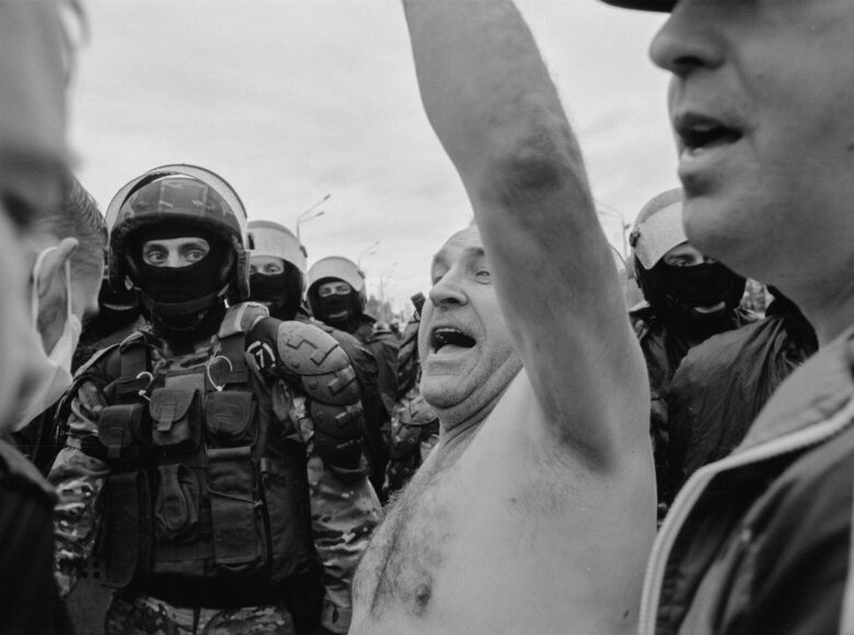 Zdjęcie wykonane przez Zmicera Waynowskiego, wykonane podczas protestów w Białorusi w 2020 roku. Przedstawia mężczyznę bez koszuli, ma otworzone usta, podnosi jedną rękę do góry. Mężczyznę otaczają żołnierze.