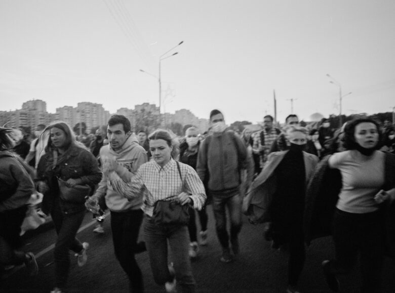 Zdjęcie wykonane przez Zmicera Waynowskiego, wykonane podczas protestów w Białorusi w 2020 roku. Przedstawia tłum ludzi biegnący przez ulice. W tle znajdują się wieżowce.