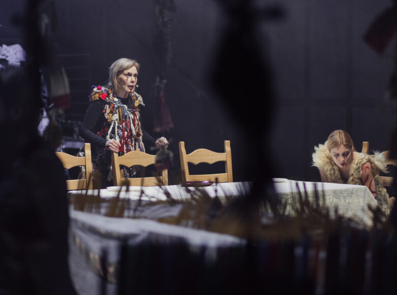 Zdjęcie. Scena ze spektaklu "Dziady". Dwie kobiety znajdują się za stołem, nakrytym białym obrusem.