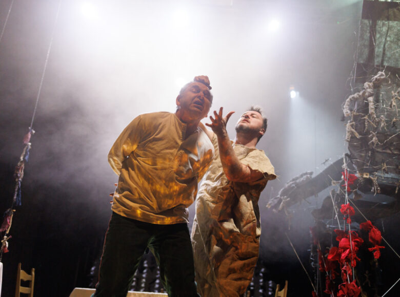 Zdjęcie. Scena ze spektaklu "Dziady". Mężczyna ubrany w płótniany worek, targa za włosy starszego mężczyznę.
