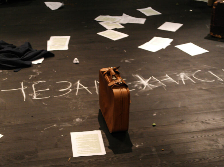 Zdjęcie. Na podłodze leżą porozrzucane, białe kartki i skórzana walizka.