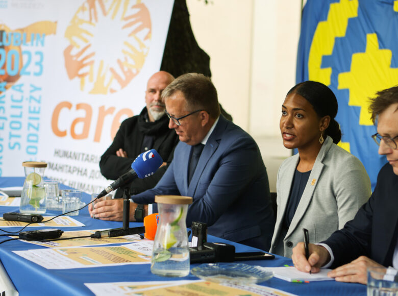 Zdjęcie z konferencji prasowej. Grupa ludzi siedzi za stołem, przykrytym niebieskim obrusem. Na stole lezą mikrofony i dyktafony.