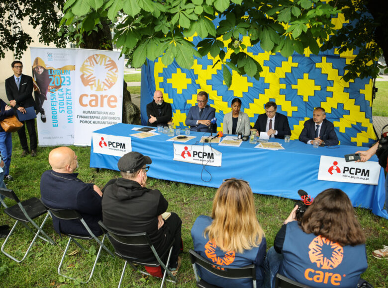 Zdjęcie z konferencji prasowej. Grupa ludzi siedzi za stołem, przykrytym niebieskim obrusem. Na stole lezą mikrofony i dyktafony.