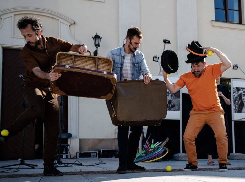 Zdjęcie. Plac przed Centrum kultury w Lublinie. 3 mężczyzn wykonuje sztuczki z piłeczkami, kapeluszami i kolorowymi obręczami.