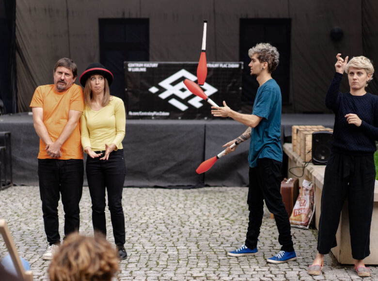 Zdjęcie. Pod Wirydarzem Centrum kultury stoi grupa ludzi, dają przedstawienie. Jedna z osób żongluje.
