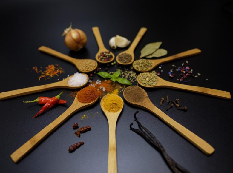Zdjęcie. Na stole lezą drewniane łyżki. Są ułożone w okręgu. Na każdej łyżce znajdują się kolorowe przyprawy.