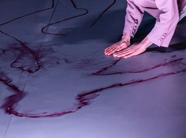 Na zdjęciu widoczne dłonie osoby, położone na płasko na szarej podłodze. Na podłodze rozmazane ślady w kolorze ciemnej czerwieni.