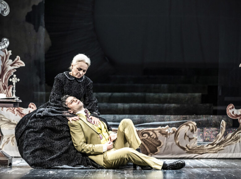 Na zdjęciu kobieta i młodszy mężczyzna. Kobieta siedzi na krześle, mężczyzna na wpół siedzi, oparty plecami o nogi kobiety.