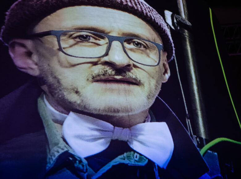 Zbliżenie na wizerunek twarzy mężczyzny w okularach widocznego na ekranie.