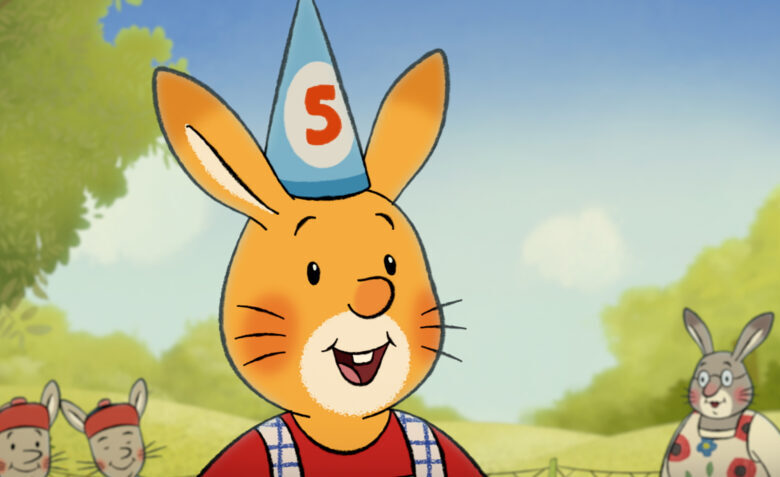 Na zdjęciu kadr z animacji przedstawiający uśmiechniętego tytułowego Królika, na jego głowie urodzinowa czapeczka z cyfrą „5”, wokół zebrane inne zwierzęta, w tle zielony plener, pola.