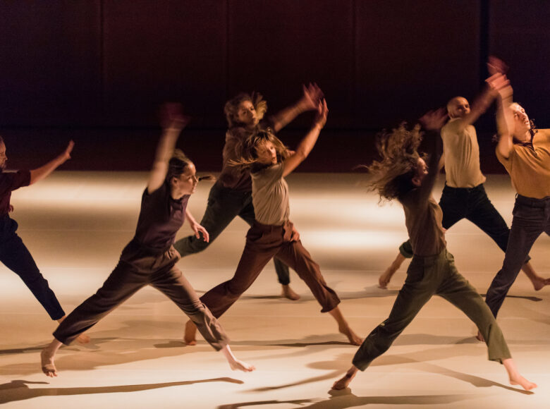 Dynamiczna kolorowa fotografia. Kilka młodych osób na scenie jednocześnie podskakuje w rozkroku. Wszyscy są ubrani w luźne ubrania.