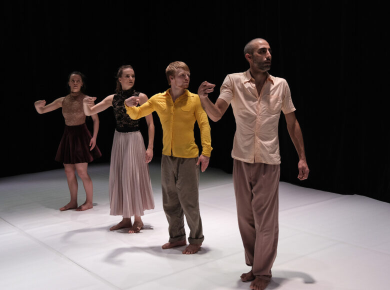 Kolorowa fotografia. Na scenie w jednym rzędzie stoją 4 osoby: dwie kobiety i dwóch mężczyzn. Wszyscy zwróceni są w lewą stronę a prawe ręce mają uniesione przed sobą w geście wskazującym. Scena oświetlona dość jasnym światłem.