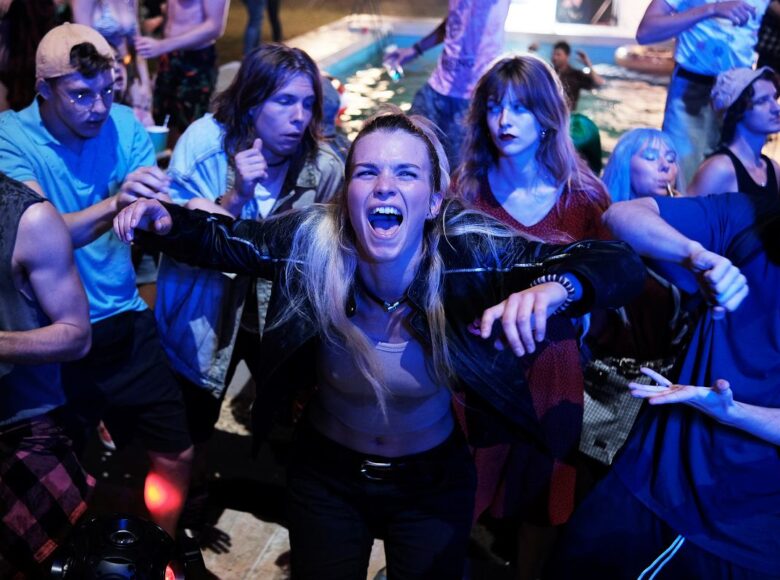 Kadr z filmu. Impreza. Bawiący się, tańczący młodzi ludzie, oświetleni niebieskim światłem, w tle basem.