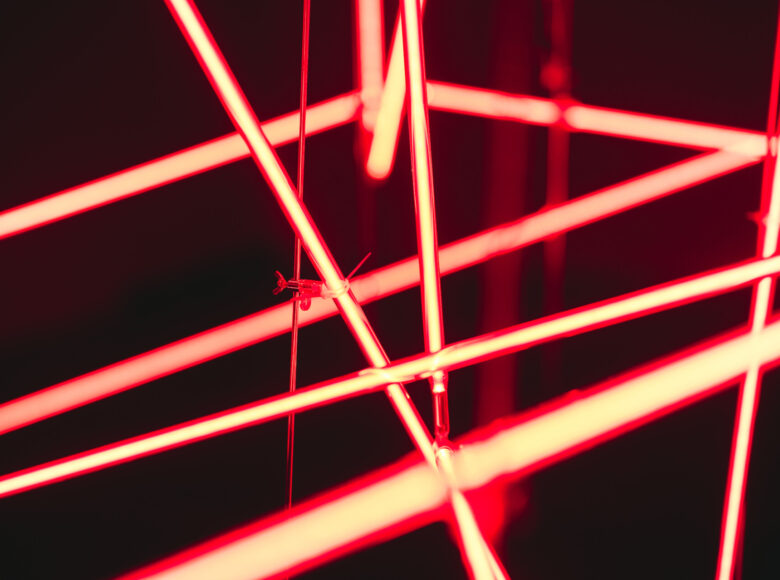 Zdjęcie. Wnętrze galerii sztuki. Na zbliżeniu neon składający się z czerwonych, przecinających się rurek.