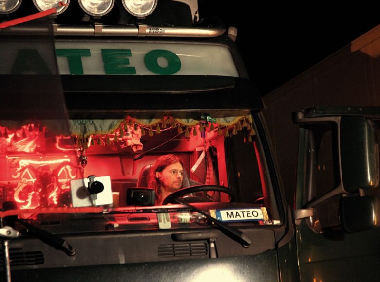 Kadr z filmu IO. Zdjęcie przestawia mężczyznę, który siedzi w kabinie ciężarówki. Na szybie ma tabliczkę z imieniem Mateo.