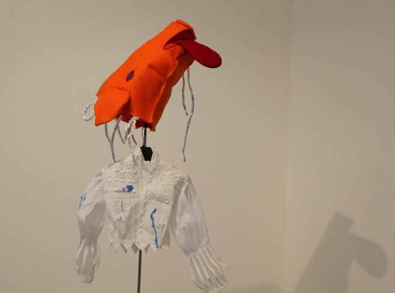 zdjecie przedstawia instalację artystyczną. Składa sie z głowy konie uszytej z pomarańczowego materiału, nabitej na drut i białe, koronkowej koszuli na wieszaku.