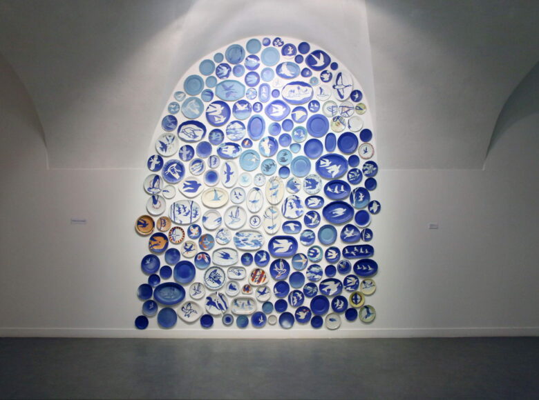 Zdjęcie przedstawia wnętrze Galerii Białej w Lublinie. Na jednej ze ścian wiszą pomalowane na niebiesko talerze z powtarzającym się na większości z nich motywem jaskółki.