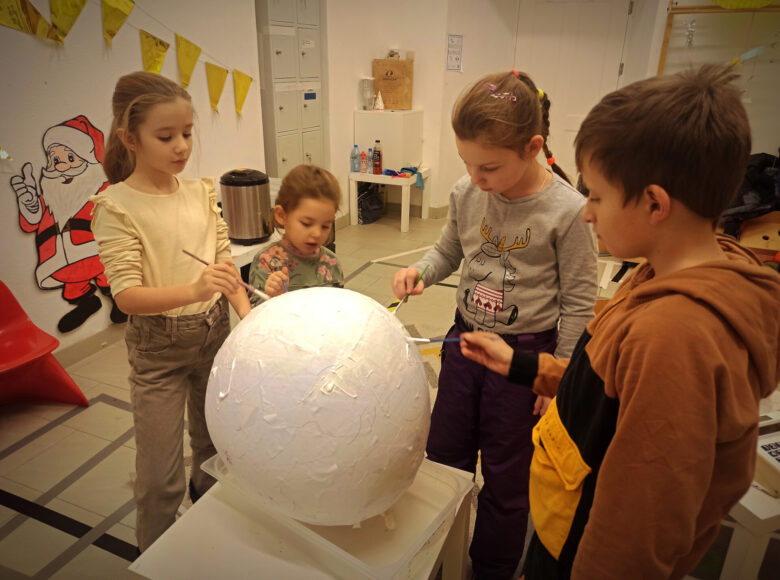 Zdjecie przedstawia grupę dzieci, która ozdabia wielką, styropianową kulę.
