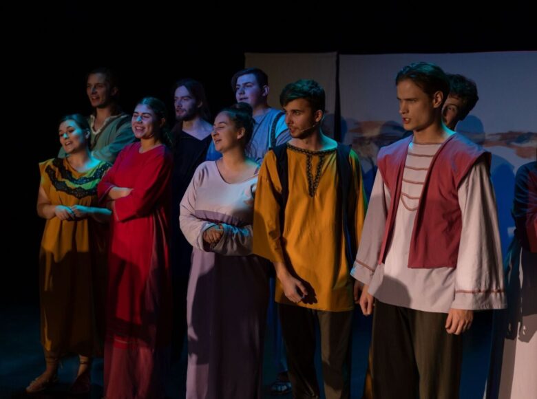 Zdjęcie ze spektaklu. Scena zbiorowa. Aktorzy stoją obok siebie i śpiewają.
