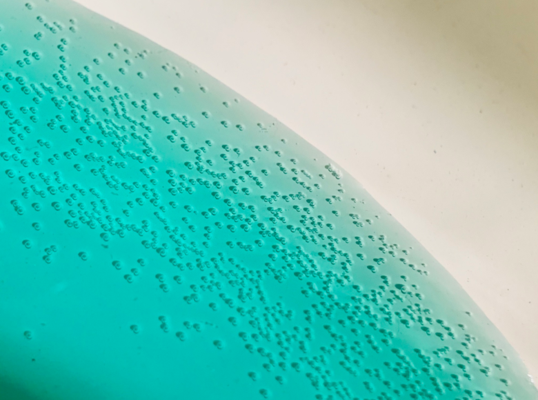 Zdjęcie przedstawia zbliżenie na niebieski płyn w białej, emaliowanej misce. Na powierzchni cieczy ukształtowały się małe bąbelki powietrza.