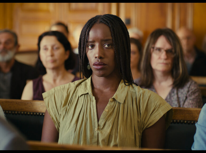 Zbliżenie na grupę siedzących kobiet. Centralnie na zdjęciu czarnoskóra kobieta, jej twarz okalają warkoczyki.